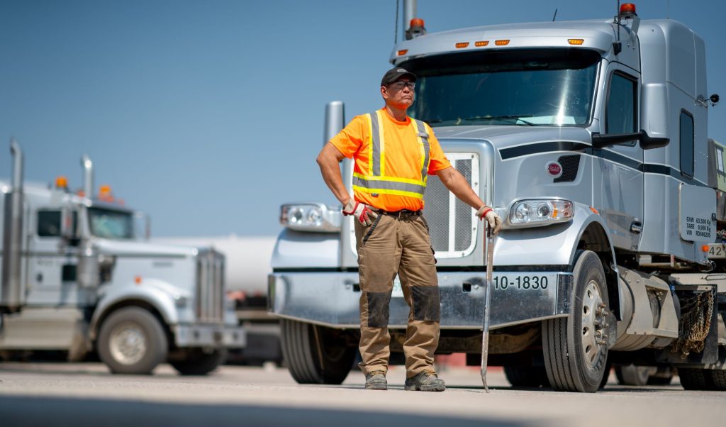 driver standing with tool in front of truck