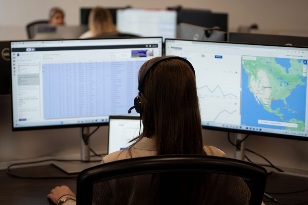 Back of woman's head in an office as she looks at two monitors with data and a map